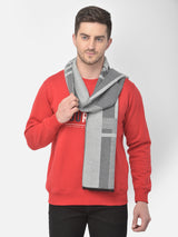 Man wearing a light grey and dark grey checked muffler with a red sweatshirt on a light background.